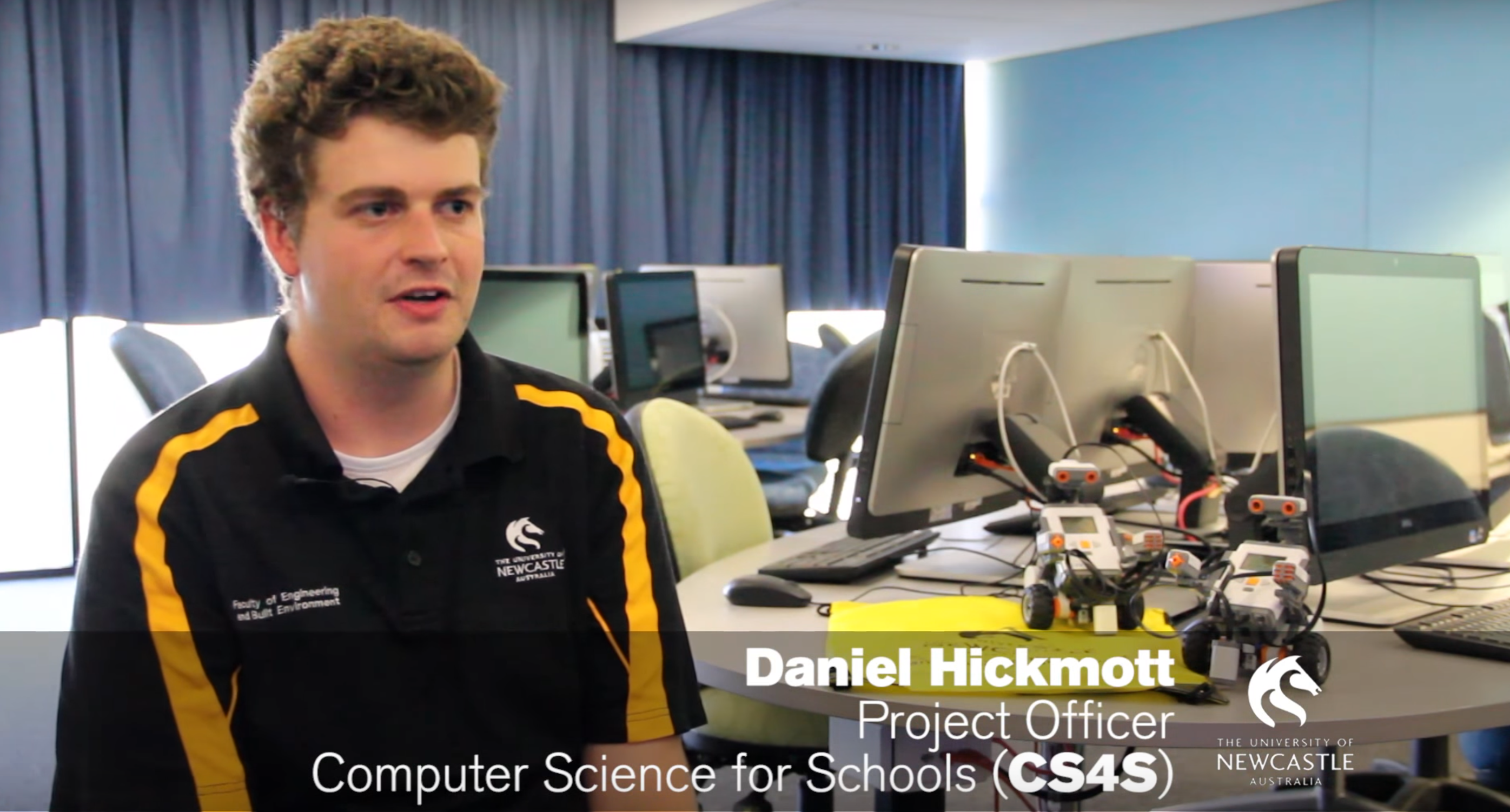 A frame from a video that shows a man (Daniel Hickmott) in front of computers in a computer lab.